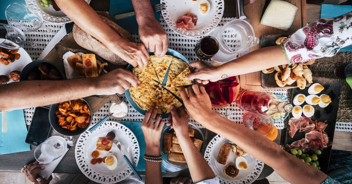 a table with food where a group of hands is grabbing the food
